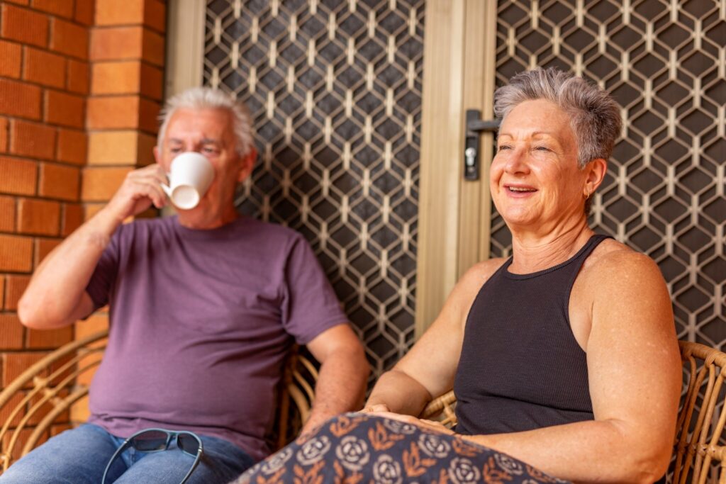 A woman and a man sitting on their front porch having a cup of tea.