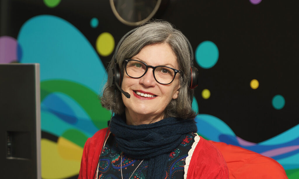 Receptionist at Wellways wearing a headset sitting in front of wall mural