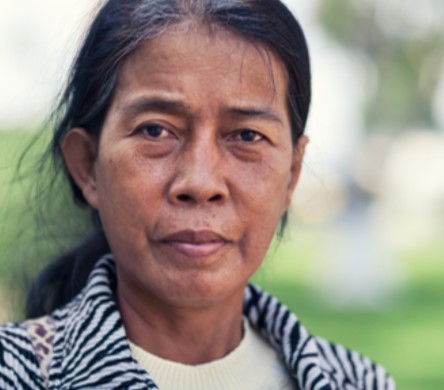 A portrait of a cambodian woman with a serious look on her face with trees and grass in the background