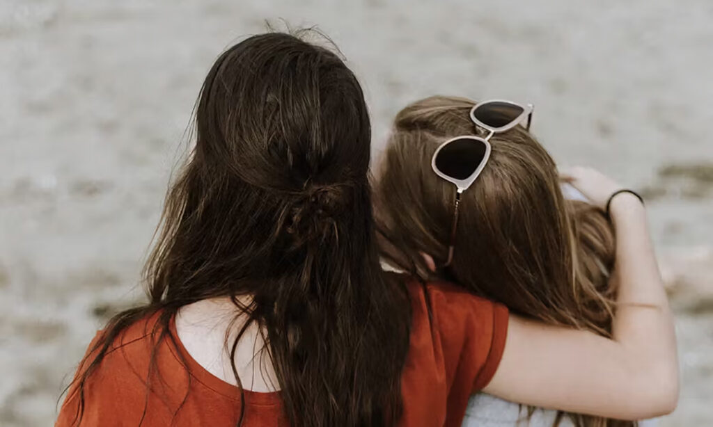 Two girls sitting on the beach holding each other in support