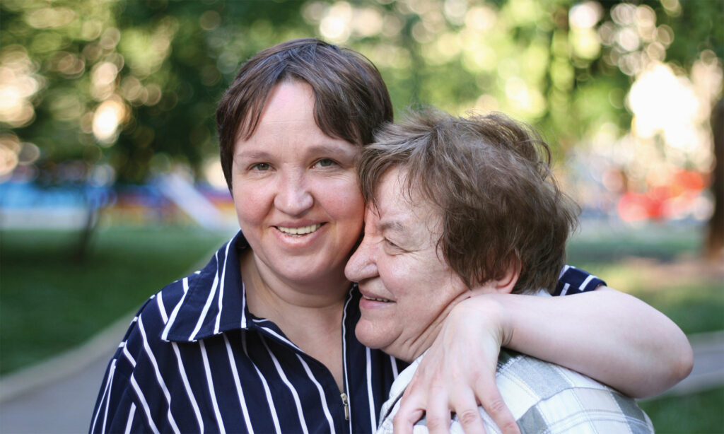 An elderly mother and her middle aged daughter hugging in a park
