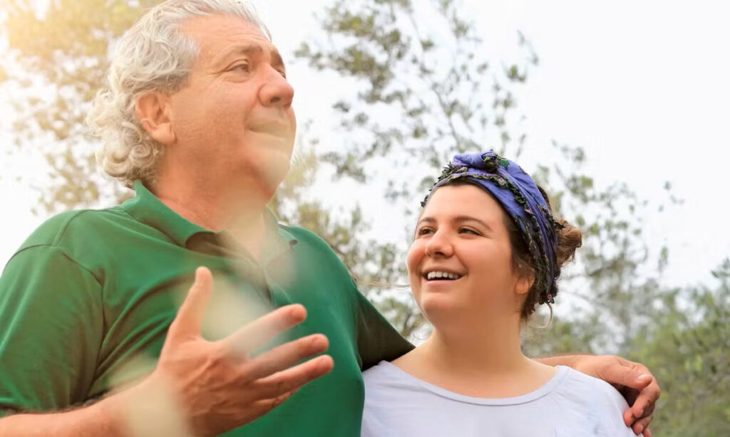 A father and daughter laughing together with trees and sky in the background