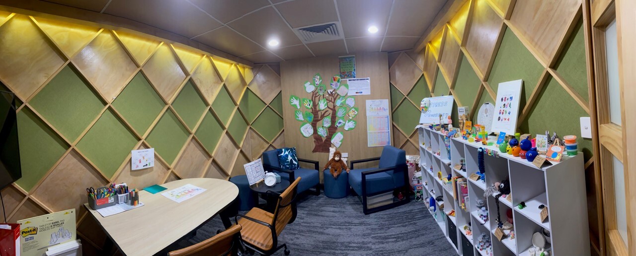 Panoramic view of a room with decorated walls, chairs, a bookshelf full of games and a table.