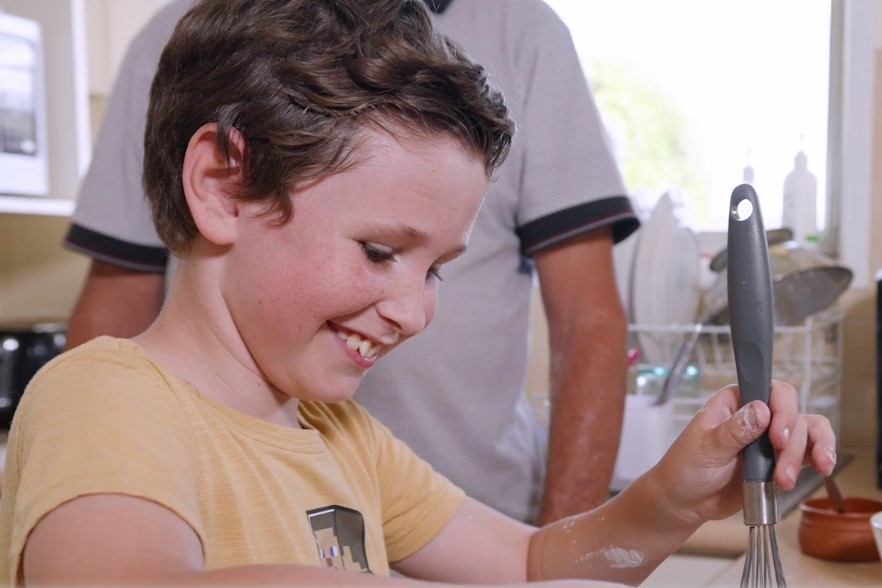 Young boy in the kitchen mixing pancakes in a bowl.