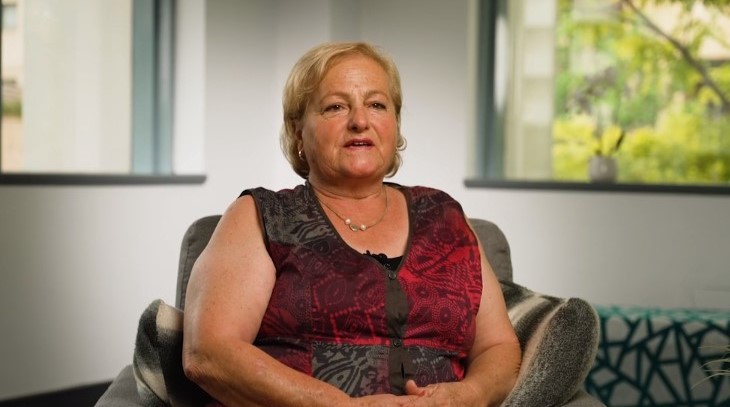 Mary, a carer sitting in a chair in a room being filmed for an interview wearing a red shirt.