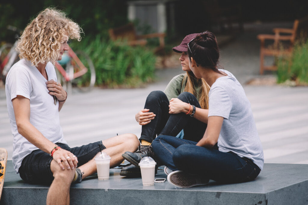 Three students hanging out on a concrete ledge in an urban setting