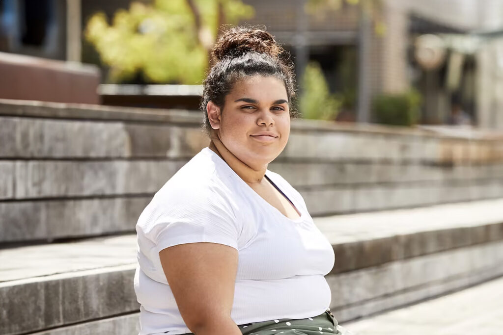 An Aboriginal woman sitting on concrete stairs smiling toward the camera