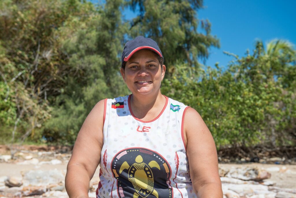 A First Nations person wearing a singlet on a beach smiling intentely