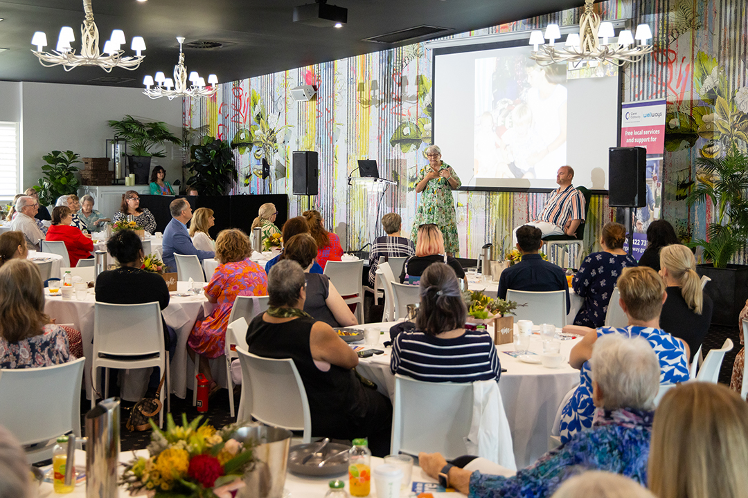 A large group of people seated around tables in a conference room during an event