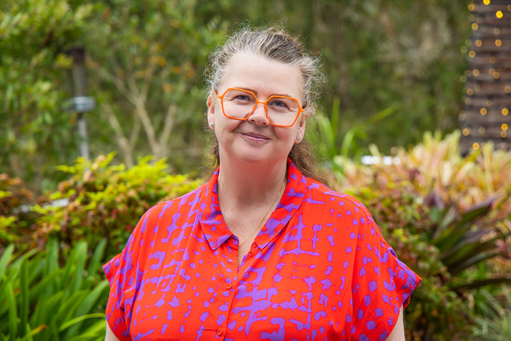 A person wearing brightly coloured clothes and glasses in a garden