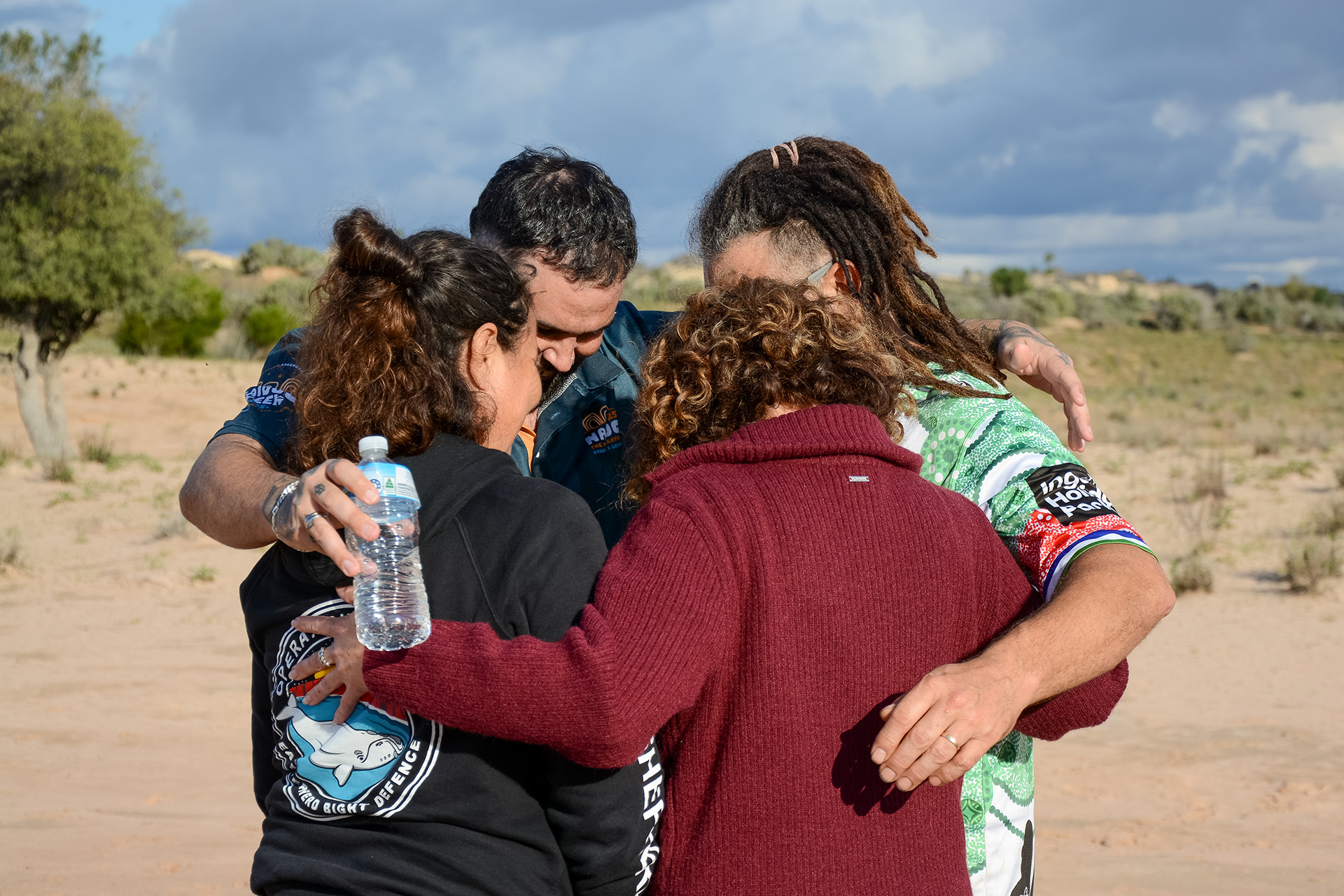 A group of people standing in a circle with their arms around each other in the desert