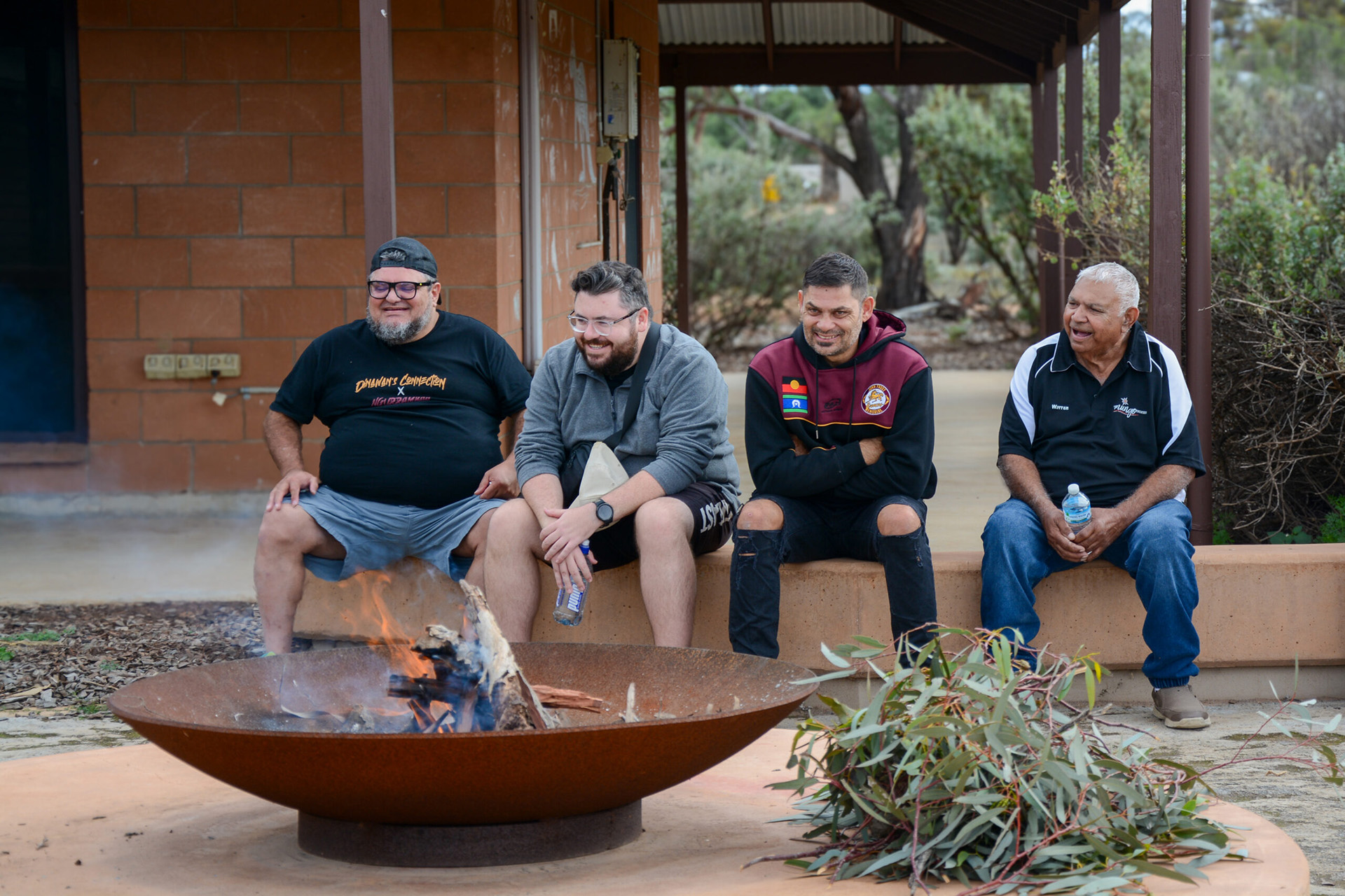 Four people sitting on a bench laughing in front of a red brick building in the bush