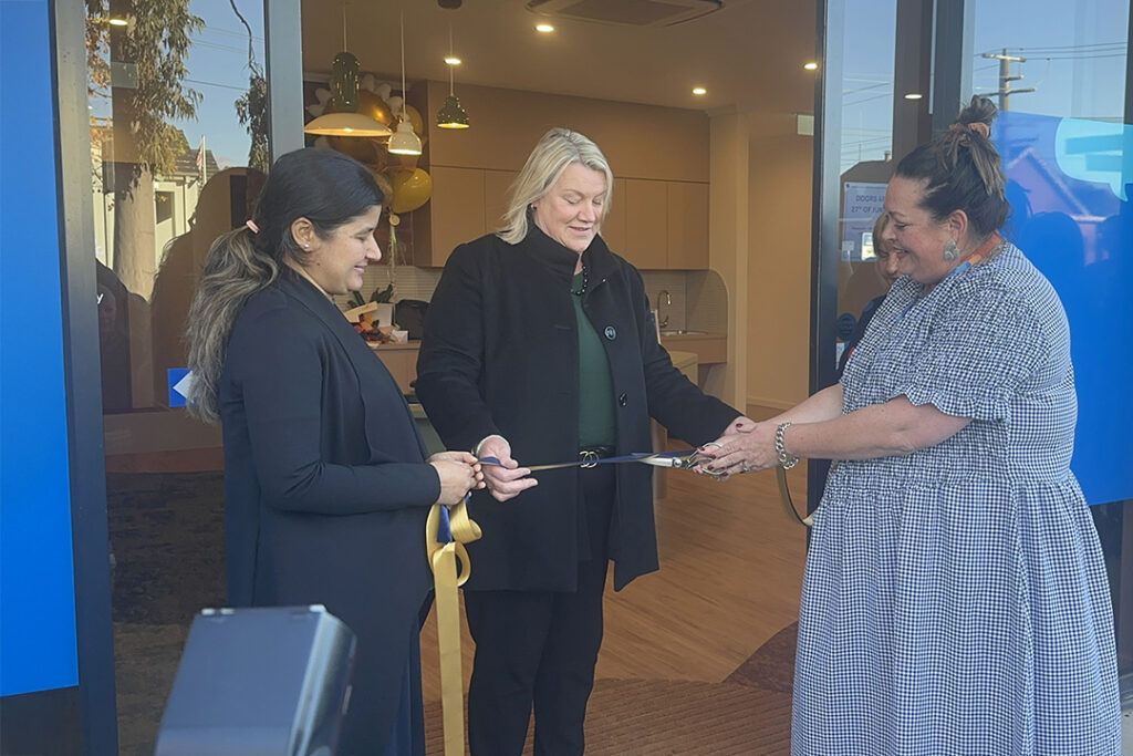 Three people in front of a building cutting a large ribbon.