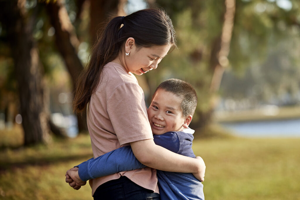 Young siblings hugging outside in the park.