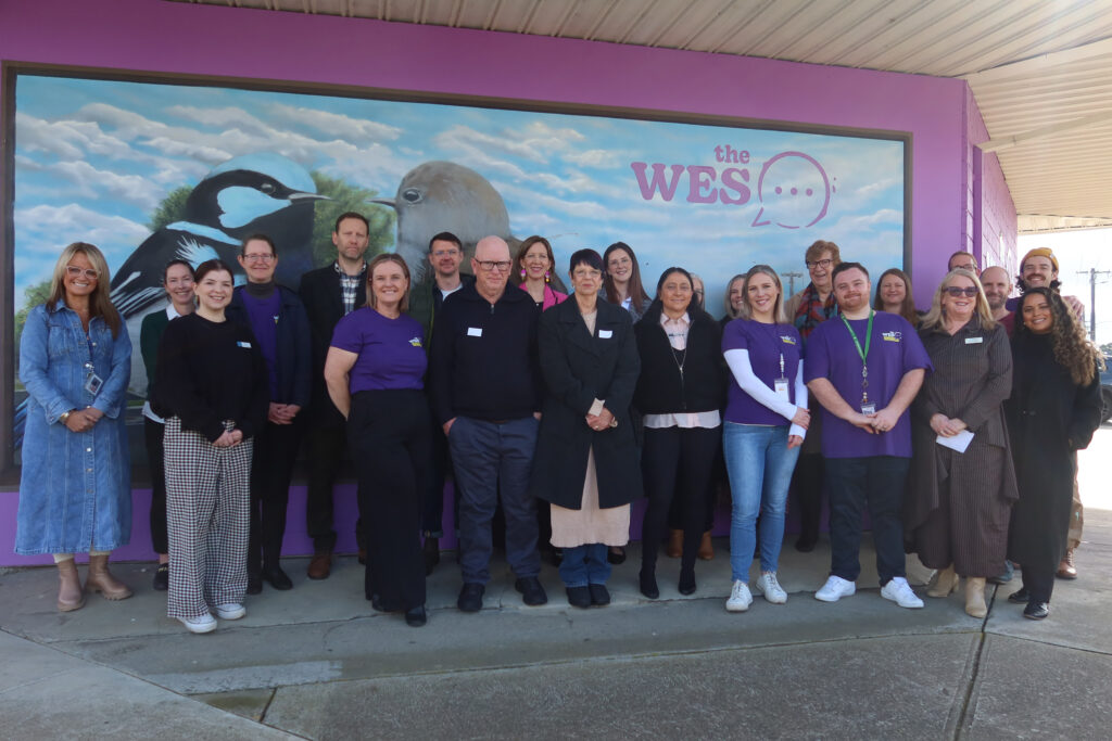 A large group of people in front of a purple wall with a painted mural