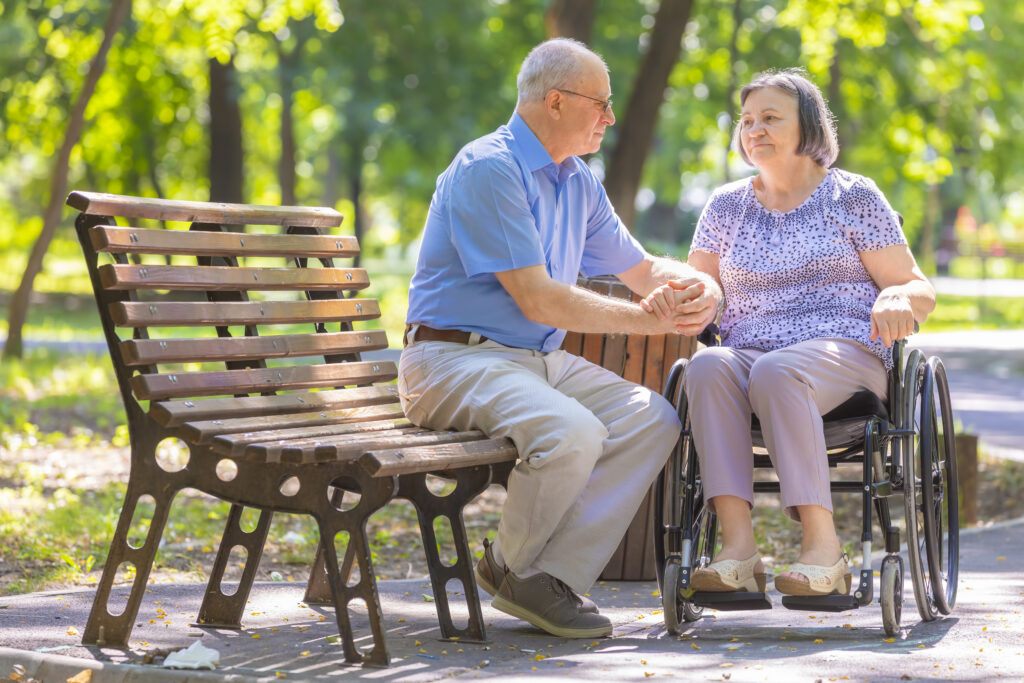 Elderly man strengthens his wife in the wheelchair outside the summer park.