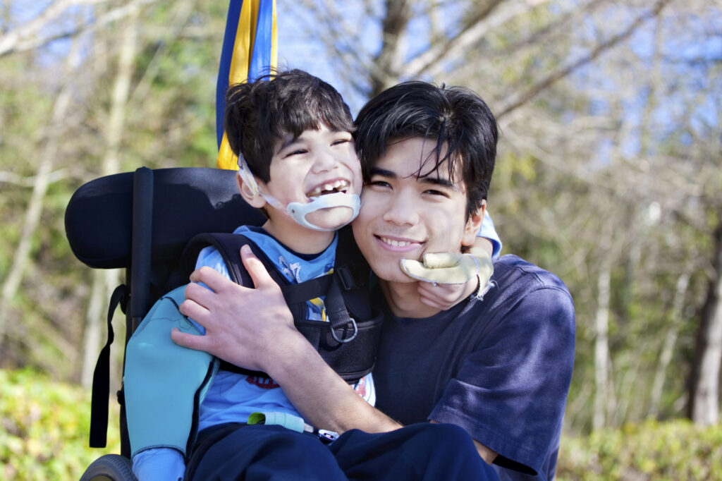 A happy adult embracing a laughing child who is in a wheelchair in an outdoor setting