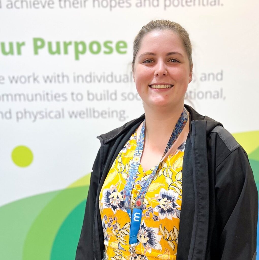 Person smiling at camera in front of a wall with Wellways signage.