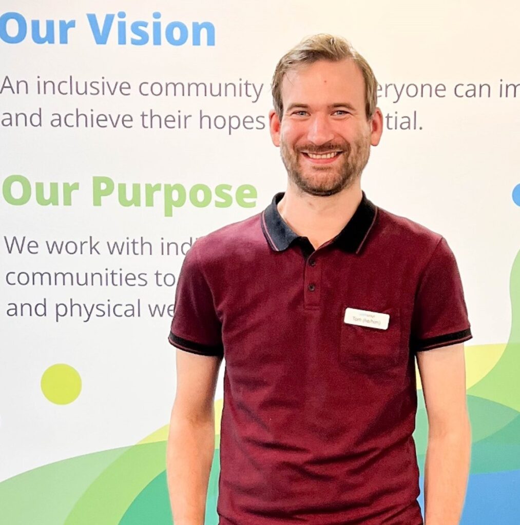Person smiling for camera in front of a wall with Wellways signage.