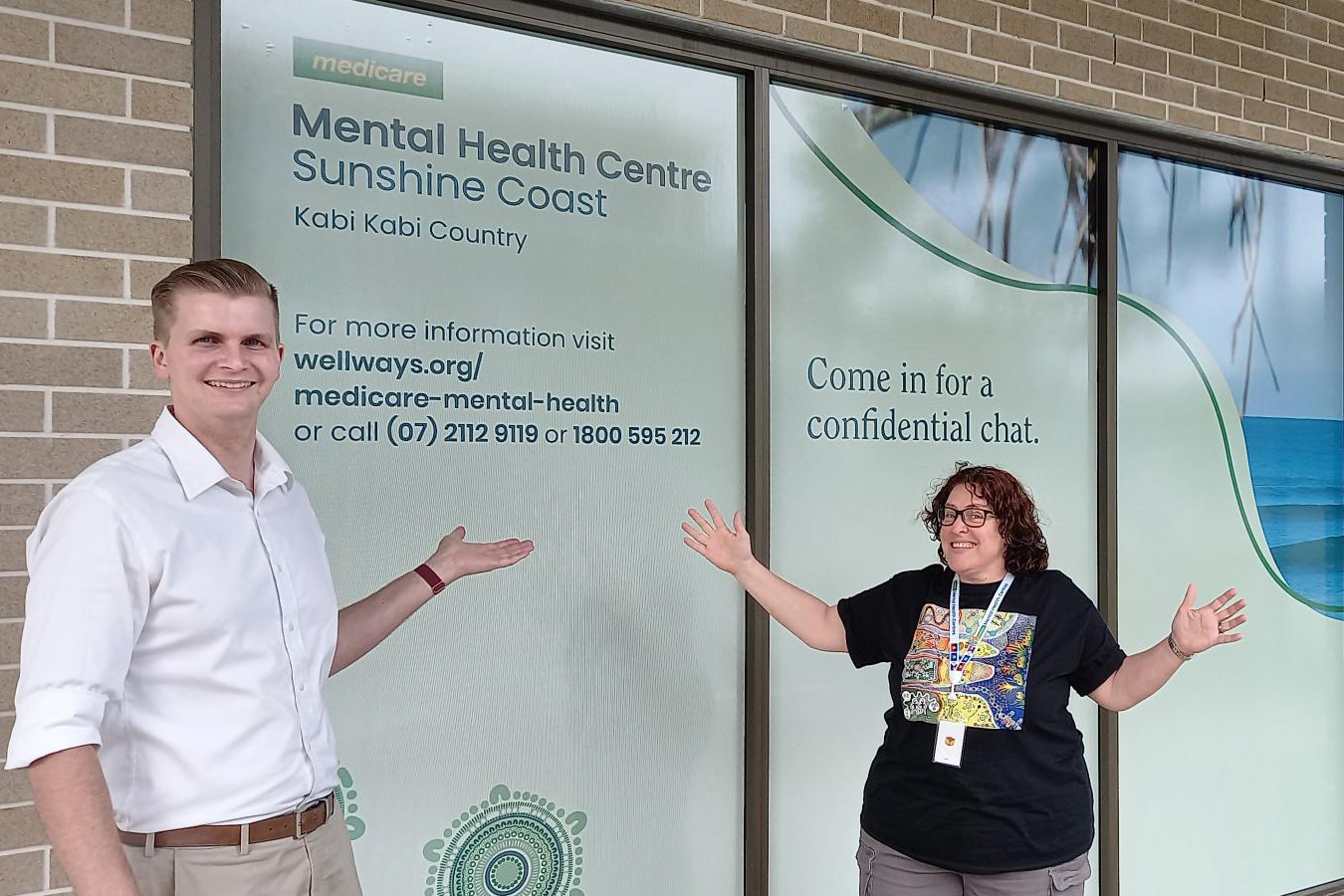 Two people posing in front of Medicare Mental Health centre signage.