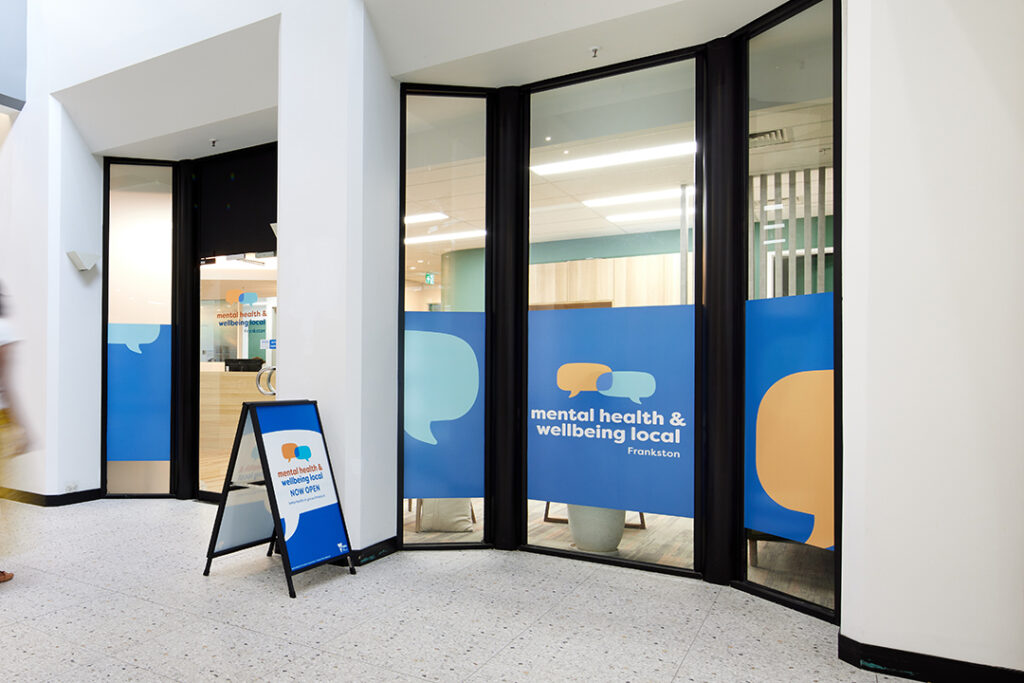 Entrance to Mental Health & Wellbeing Local - Frankston, with blue signage and an A-frame sign reading 'Now Open'.