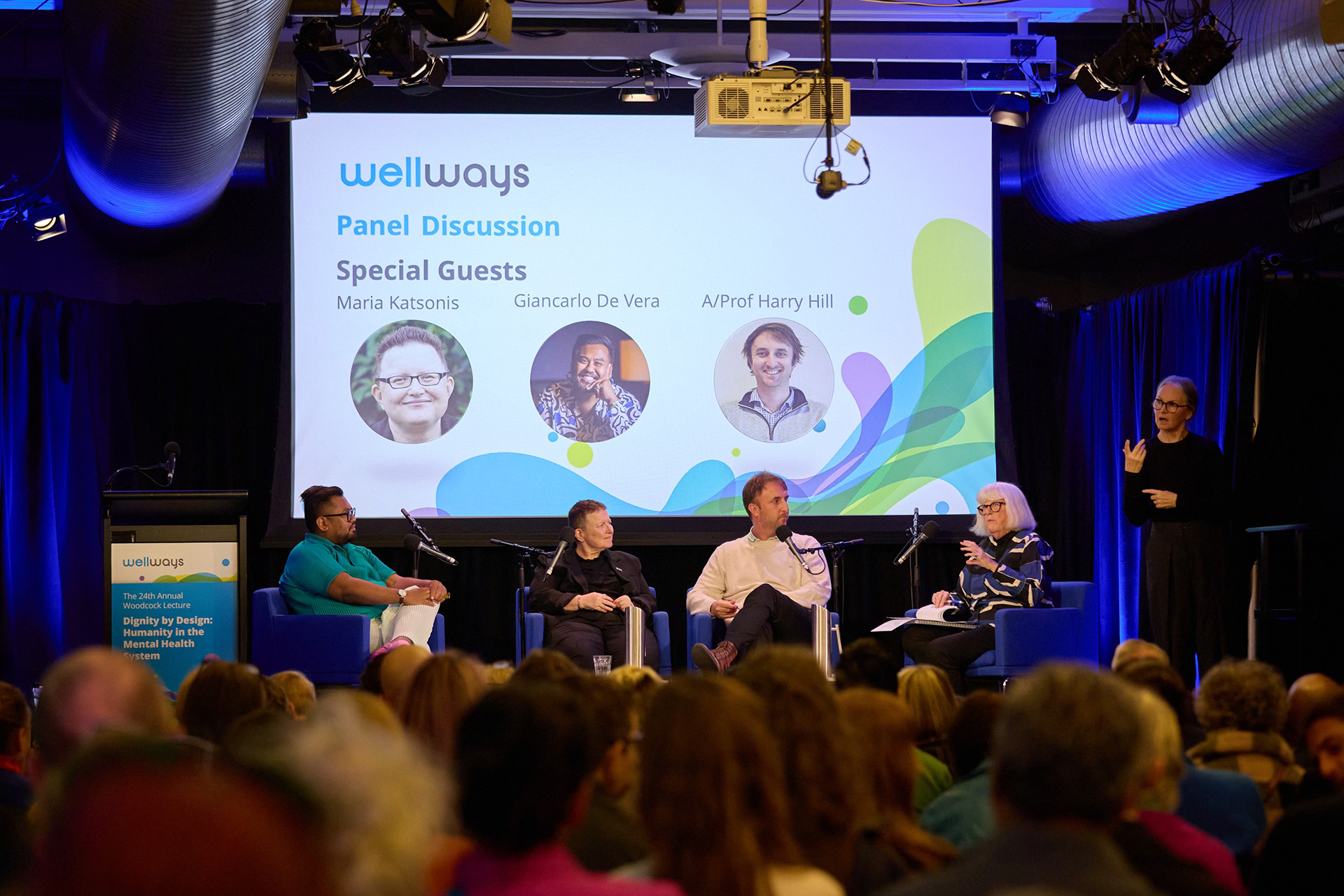 A large crowd of people watching four people and an interpreter on a stage.