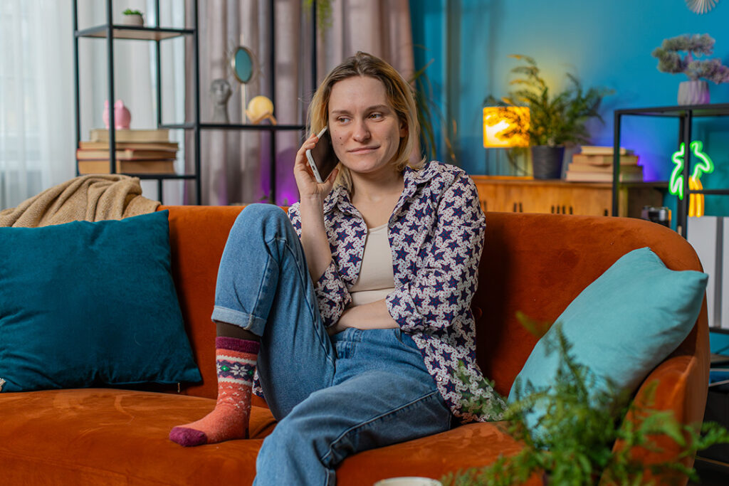 A young person wearing Jeans and colourful socks sits on an orange couch.
