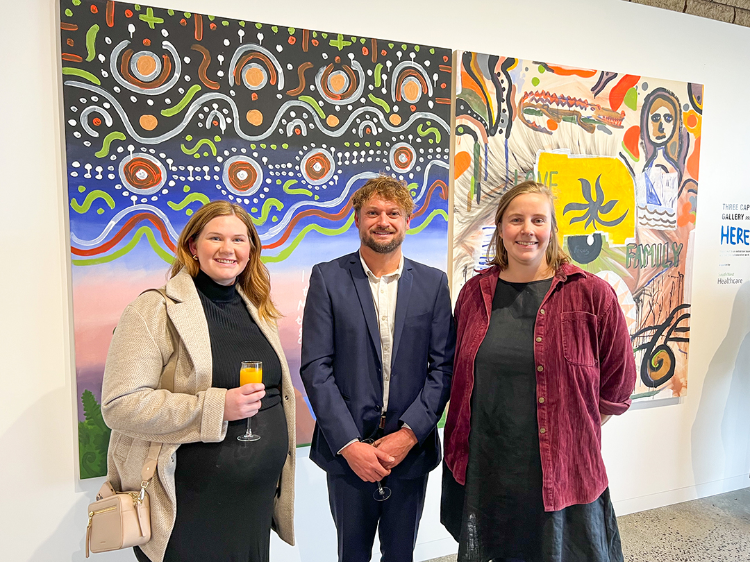 Three people standing in the middle of a room with artwork on the walls behind.