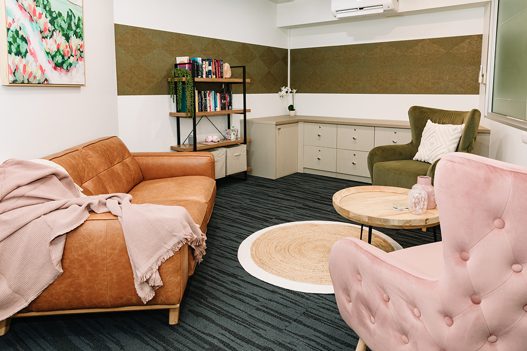A well lit room with an brown leather lounge, pink velvet armchair and grey carpet.