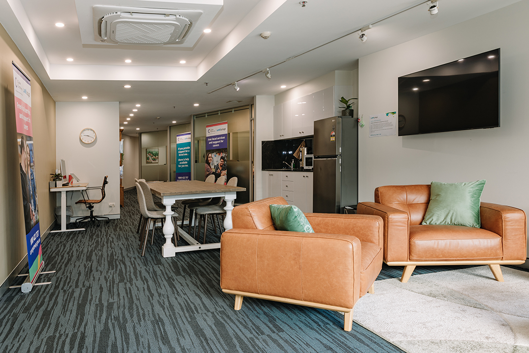 A large room with brown leather seats, an island bench, wall mounted televisions and a kitchenette.