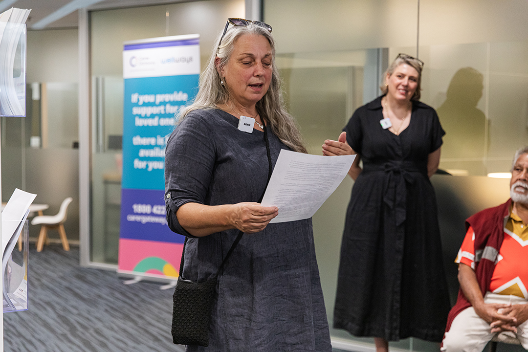 A person looking at a piece of paper and speaking, while another person watches in the background.