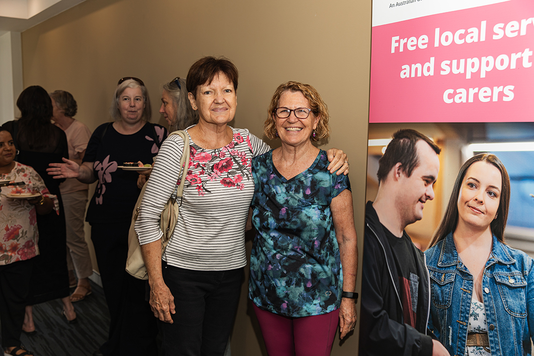 Two people standing next to a large banner with their arms around each others shoulders.