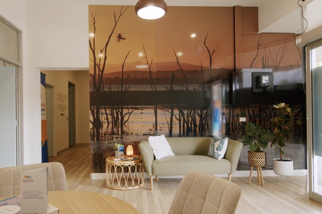 A well lit room with a couch and a large print on the wall of a wetland at sunset.