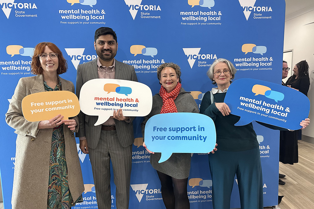Four people holding signs in front of a blue media wall.