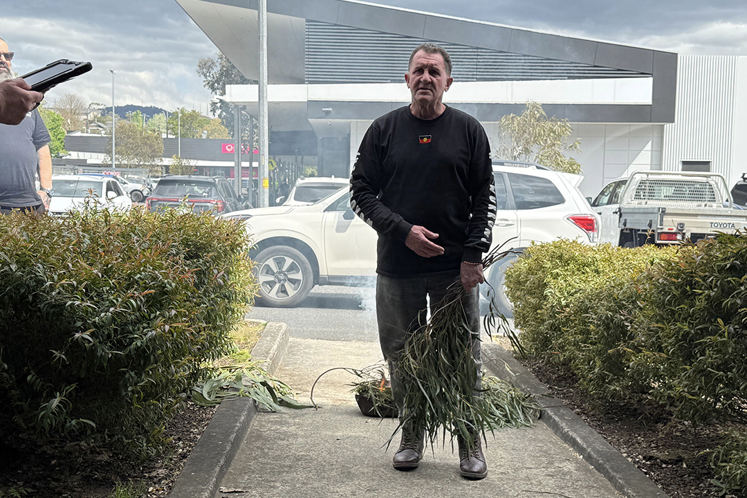 A person in dark clothing holding a eucalyptus branch on a path