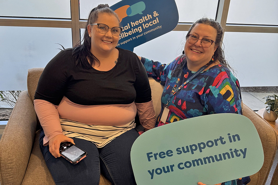 Two people sitting on a couch holding blue signs in the shape of speech bubbles.