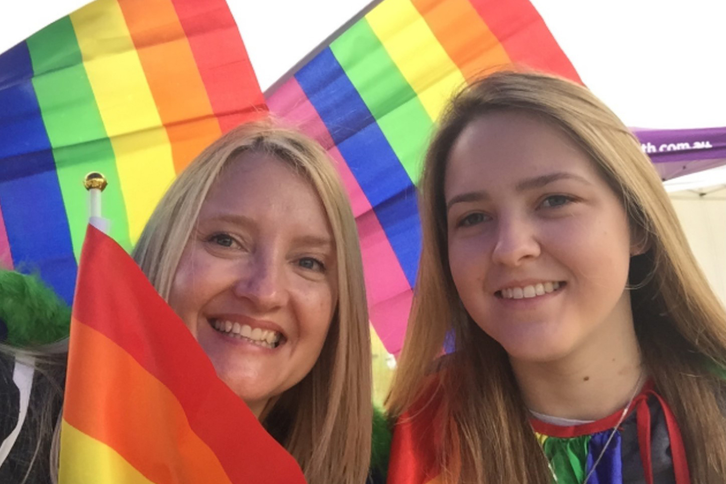 Two people surrounded by rainbow flags on a beach