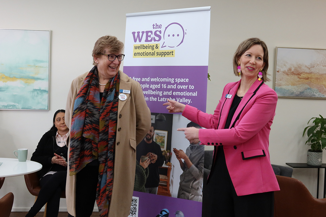 Two people in front of a branded banner speaking to a crowd
