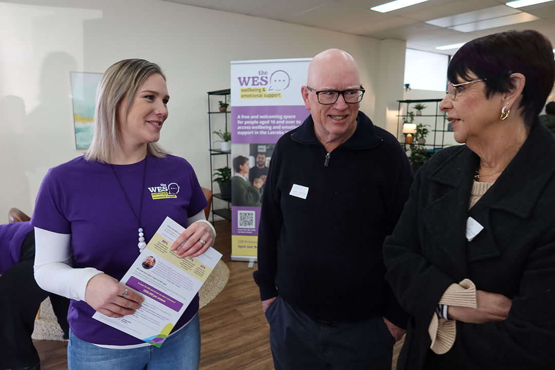 A staff member wearing purple speaks to two members of the community