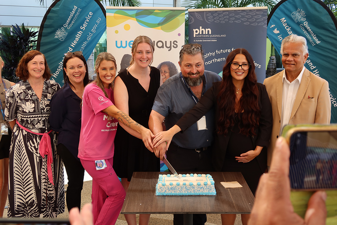 A group of people standing close together cutting a blue and white cake on a table