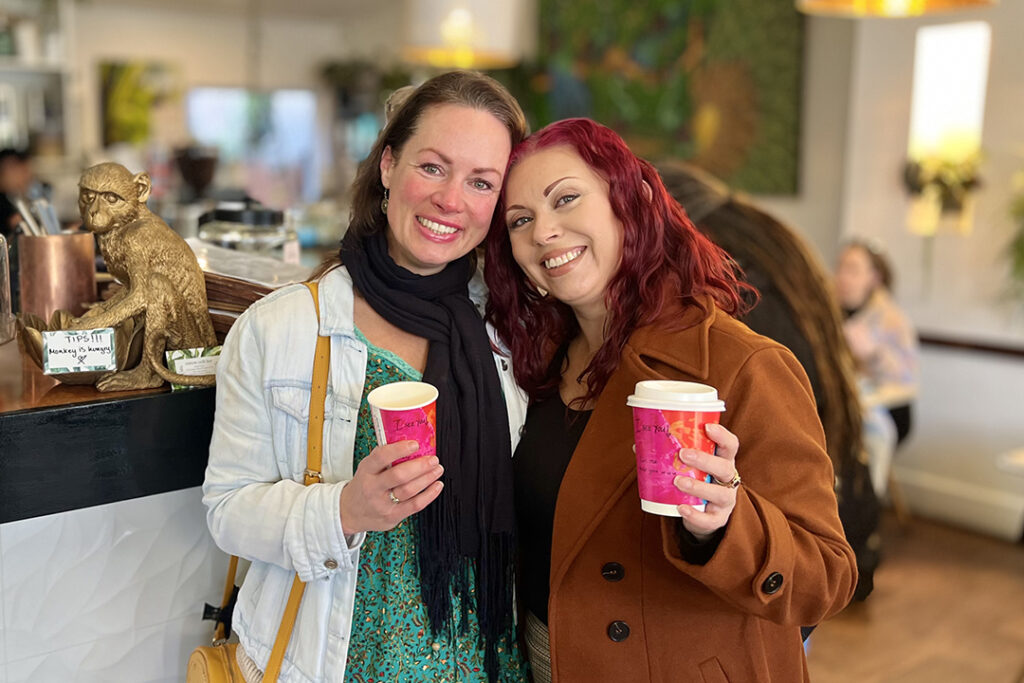 Two people standing closely in a cafe holding colourful cups.