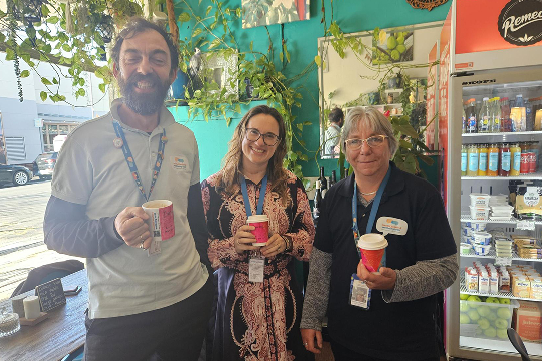 Three people standing side by side inside a cafe