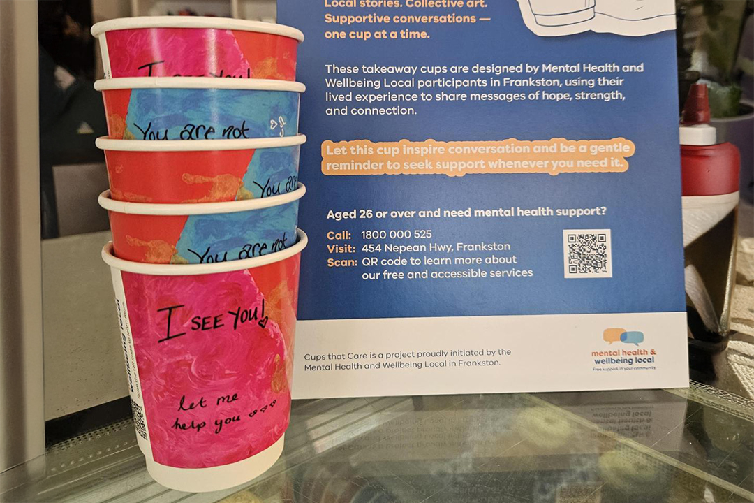Pink and blue coffee cups on a bench next to a blue sign with white text
