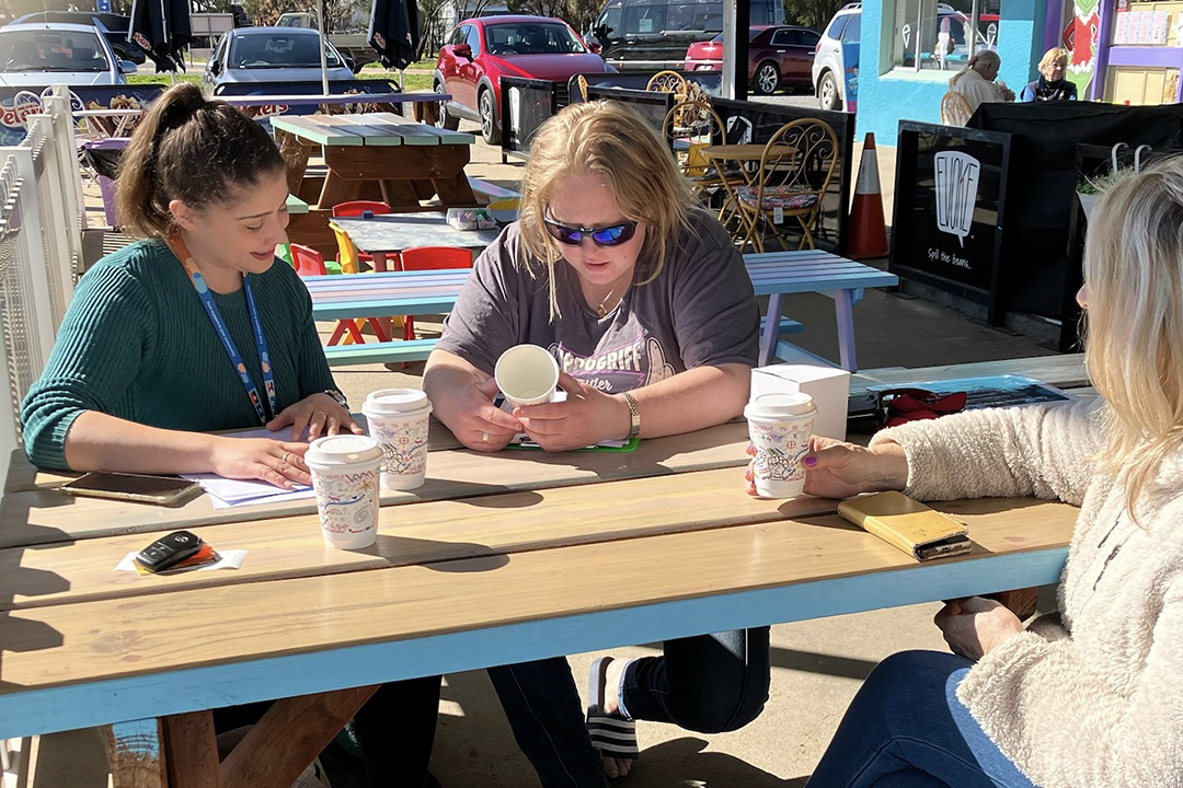 Three people sitting at an outdoor table drinking coffee