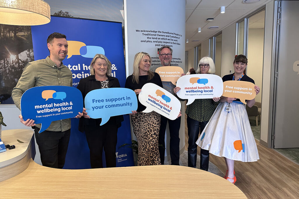 Six people standing behind the reception desk in an office space holding blue signs shaped like speech bubbles.