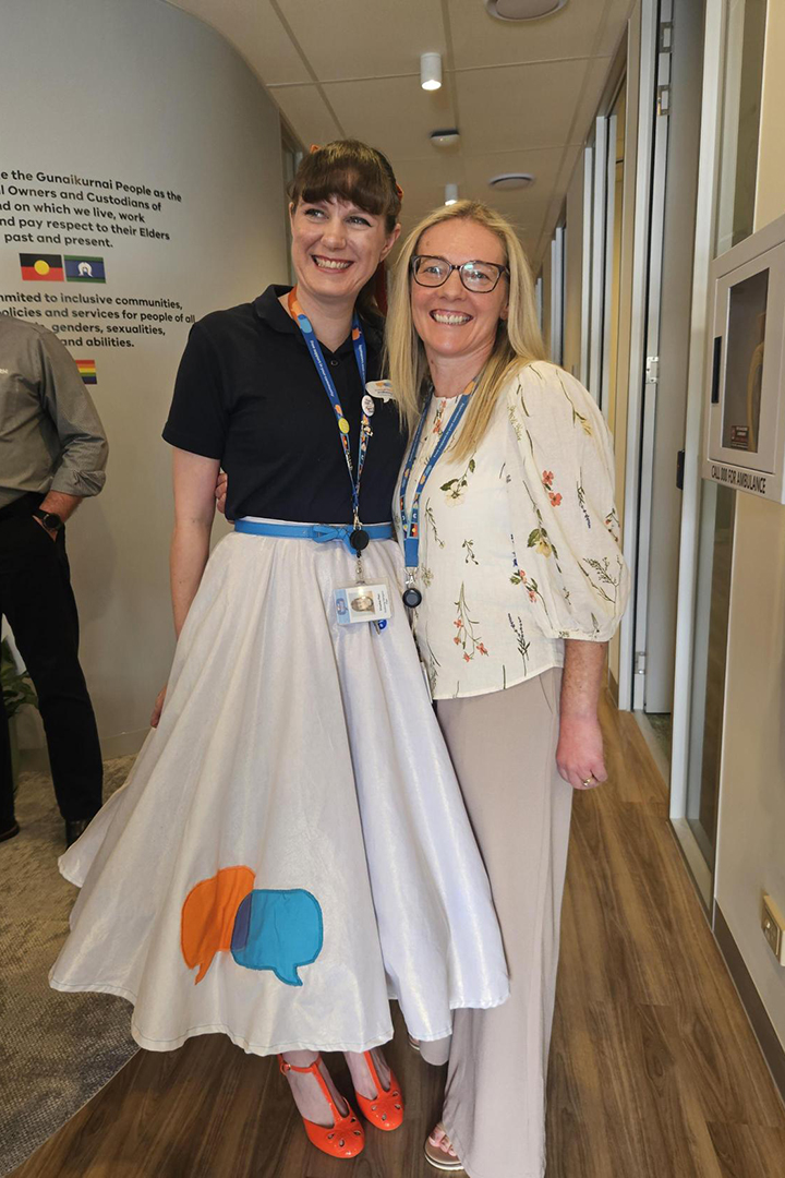 Two people standing close together in an office walkway. One is wearing a long skirt.