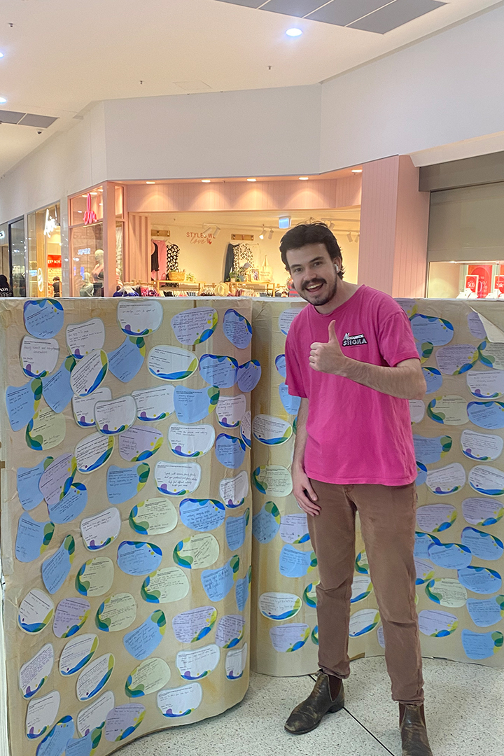 A person standing in front of a wall lined with coloured paper cutouts.