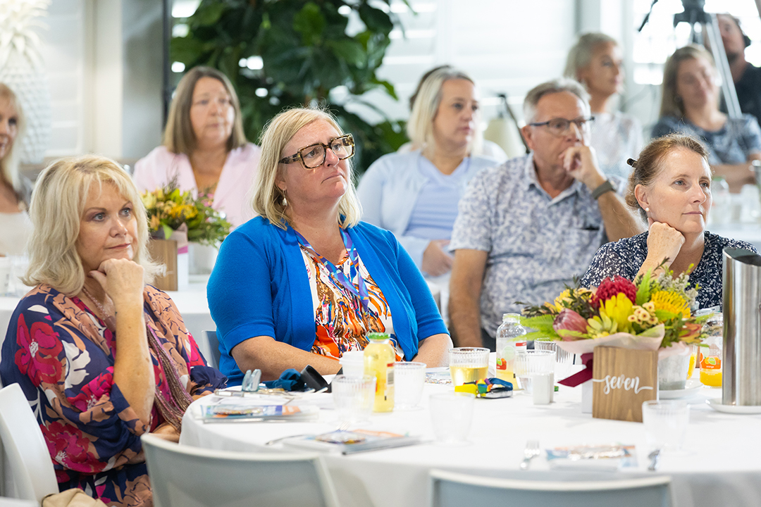 A room full of people sitting at tables with white table cloths and floral arrangements