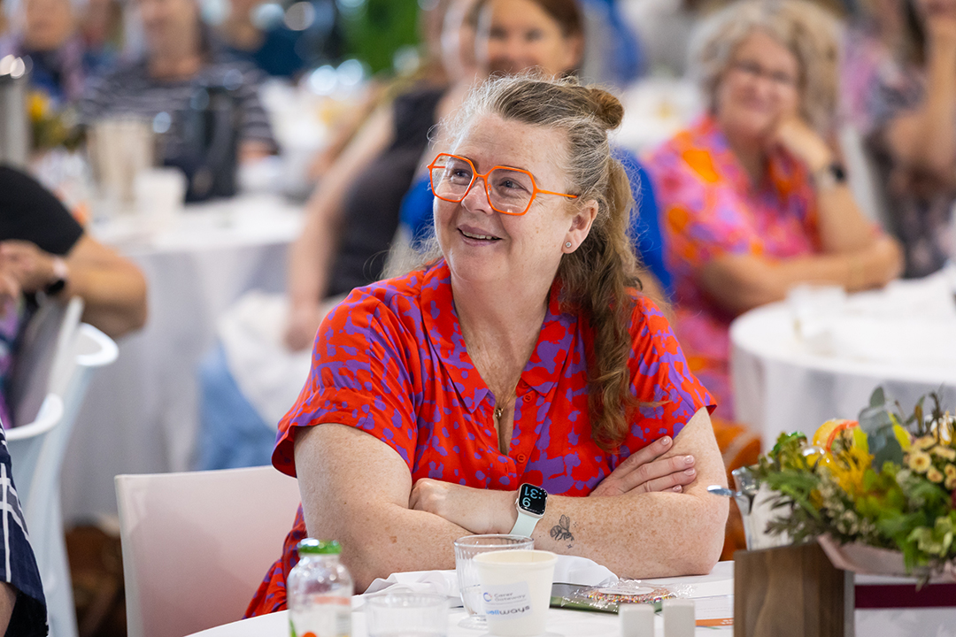 A person wearing bright orange glasses and a red and pink top at a table