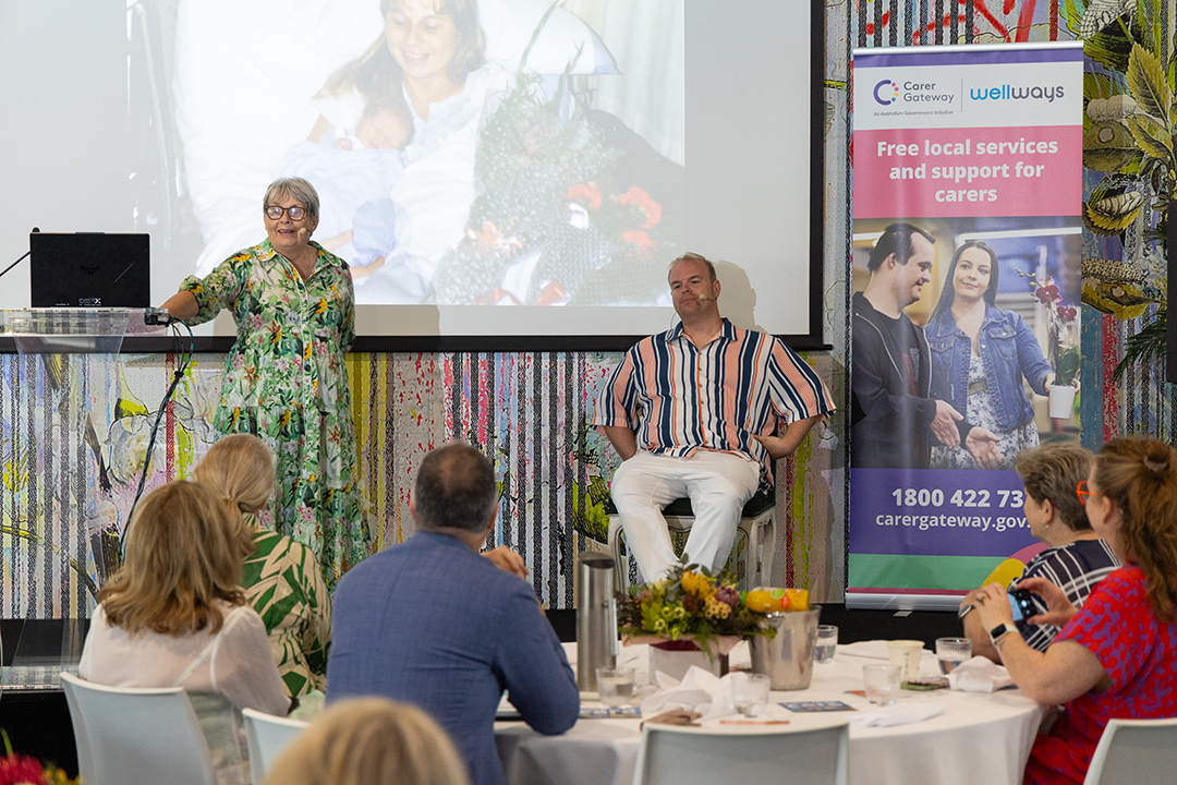Two people on stage presenting to an audience seated at a table
